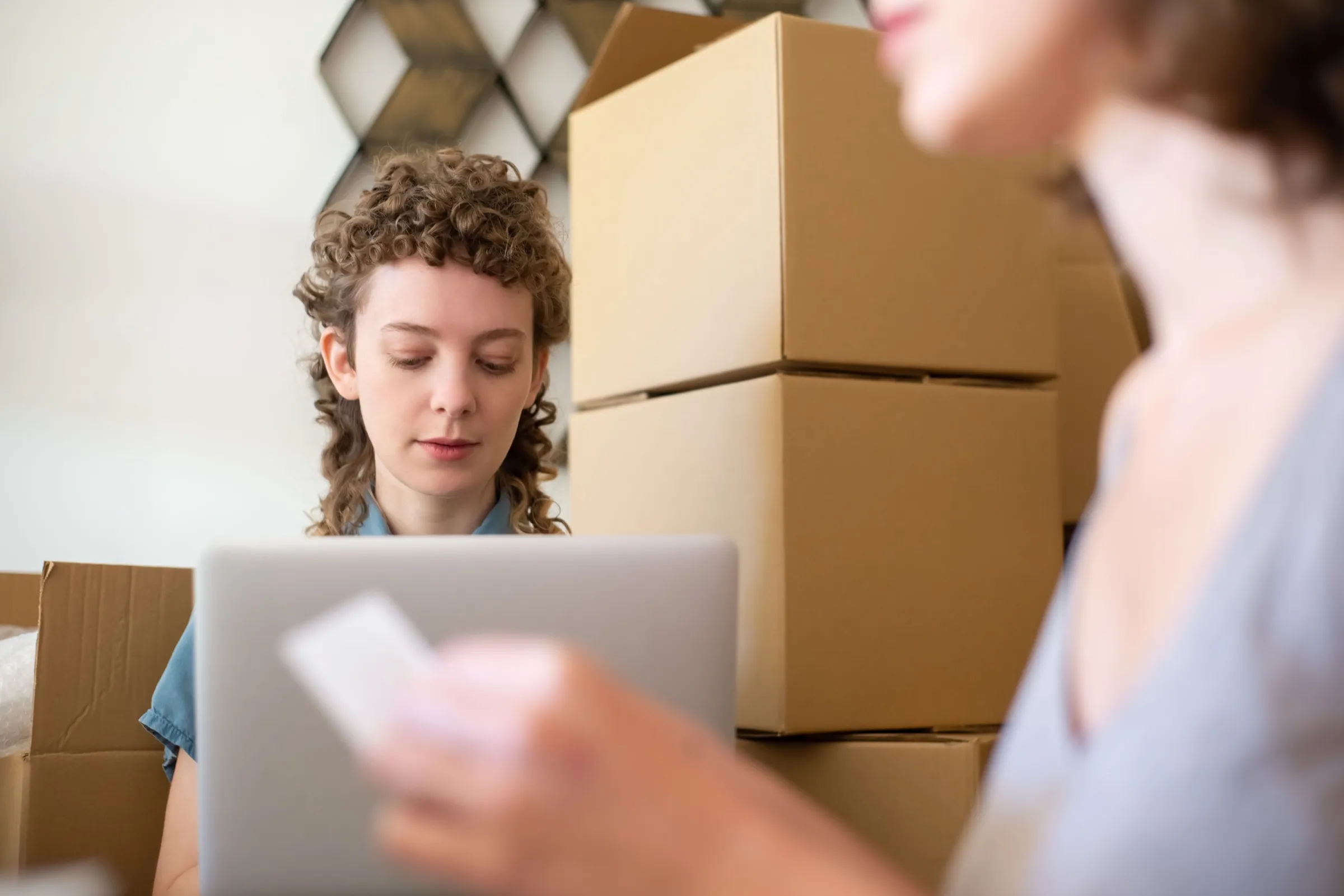 A small-business owner preparing and labeling shipping boxes at a packing station with a laptop.