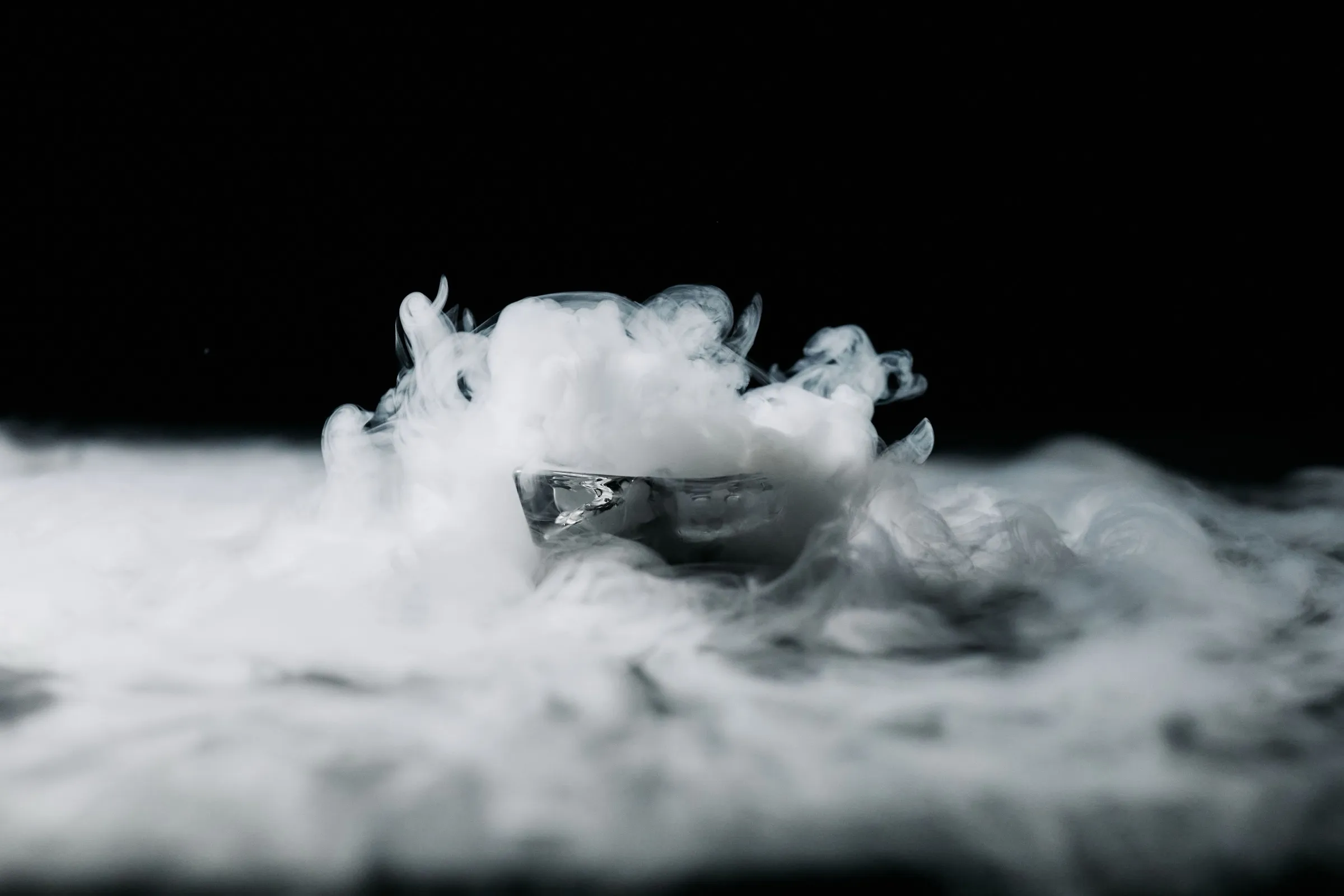 Thick white vapor of subliming dry ice rolling against a dark background.
